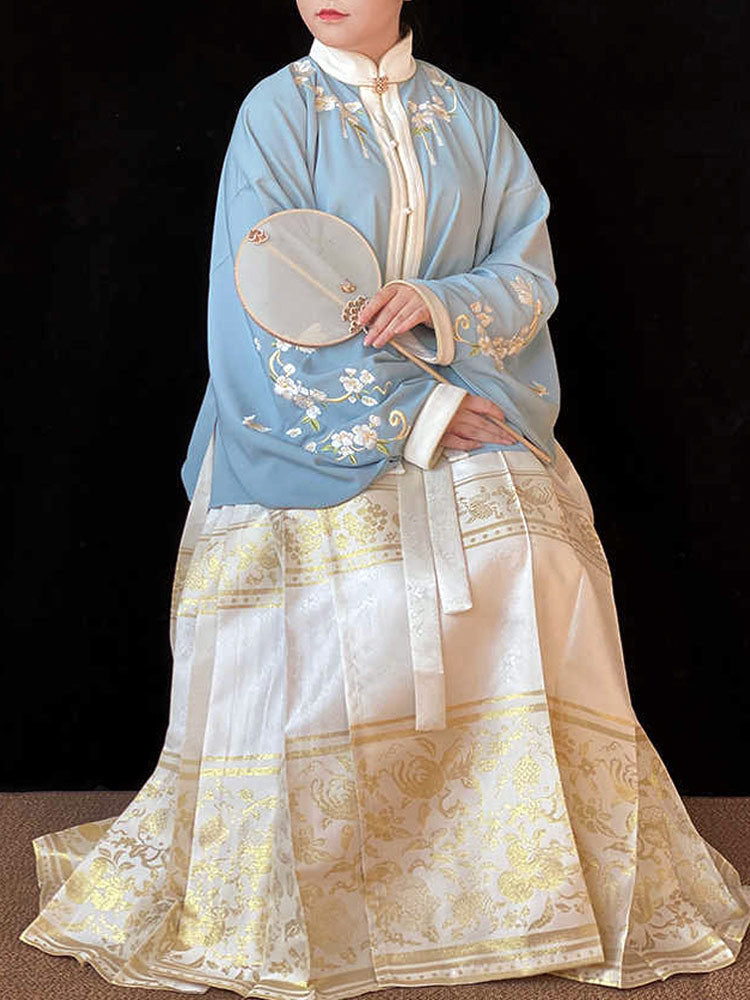 Person wearing a traditional embroidered outfit with a blue top and white skirt against a black background